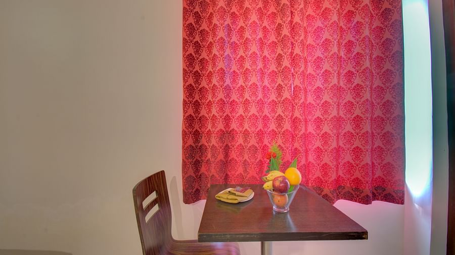 A chair, table with fruits and a curtained window | Superior Room | Woodstock Resorts, Coorg