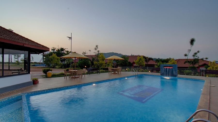Swimming pool with patios with hills in the background | Woodstock Resorts, Coorg