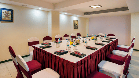 A formal boardroom set up with an elongated table covered in a red patterned cloth, surrounded by chairs at Lords Inn Vadodara.