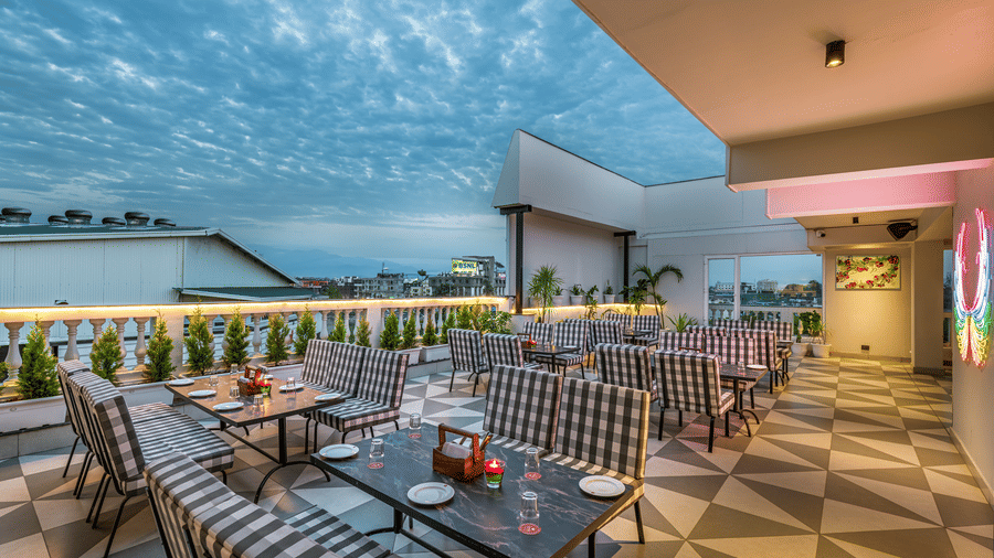 An outdoor rooftop dining area with patterned chairs and tables, set against a dramatic cloudy sky at Lords Eco Inn Dehradun.