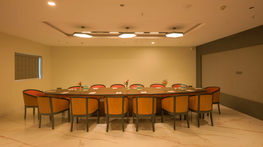 Private meeting room featuring a long conference table, orange chairs, recessed ceiling lights and a presentation screen.