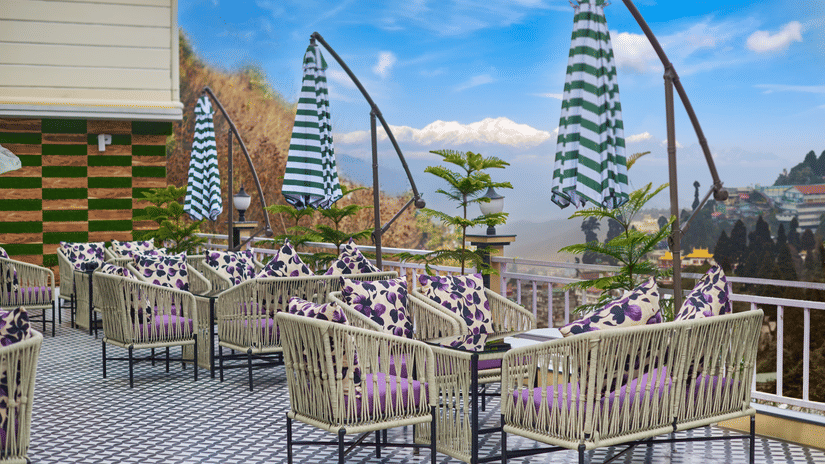 An outdoor deck with wicker seating and blue-and-white striped umbrellas under a blue sky | Voyage Rodhi Resort