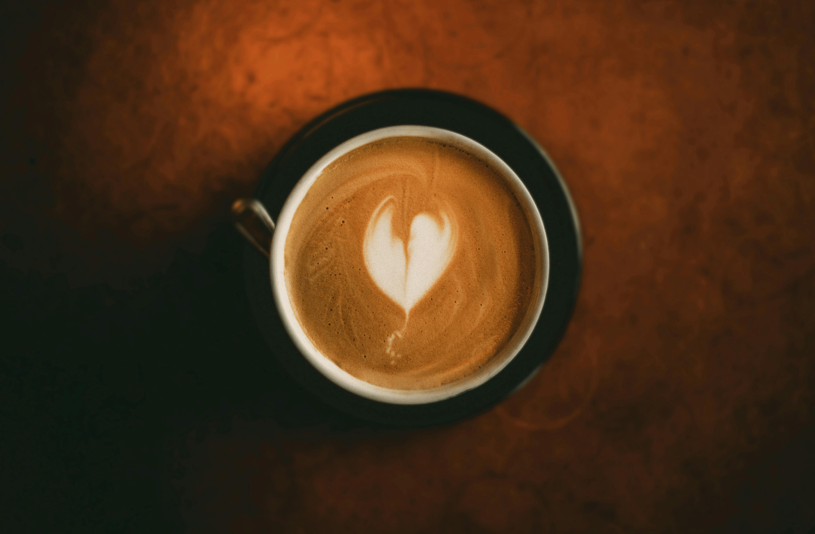 A top-angle of a cup of coffee inside a black mug and saucer