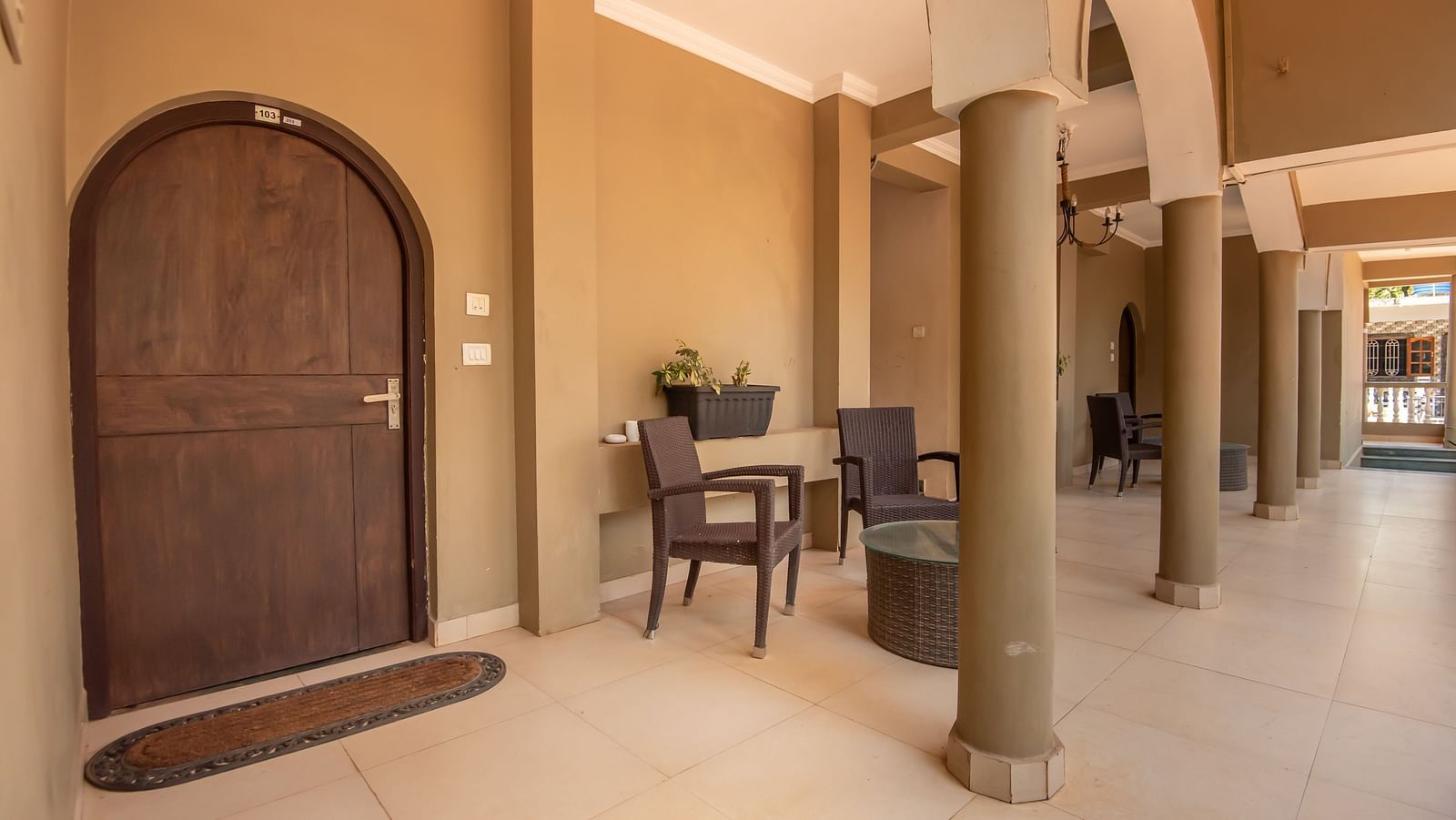 Arched wooden doorway leading to a spacious hallway with table, chairs, and warm lighting at De Soul Santé, Morjim.