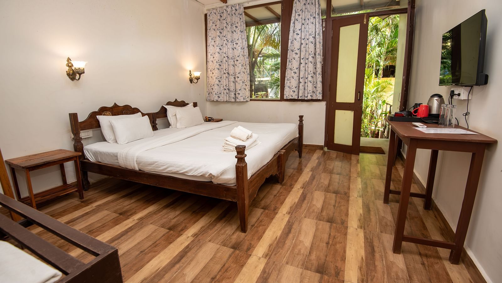 Bright guest room with a double bed, wooden flooring, a flat-screen TV, and natural light streaming in at De Soul Santé, Morjim.