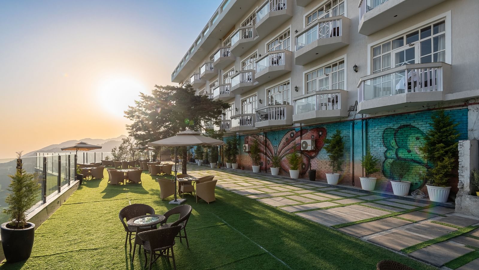 Facade view of DLS Highland Resort and Spa, Mussoorie with comfortable chairs in the lawn at dusk.