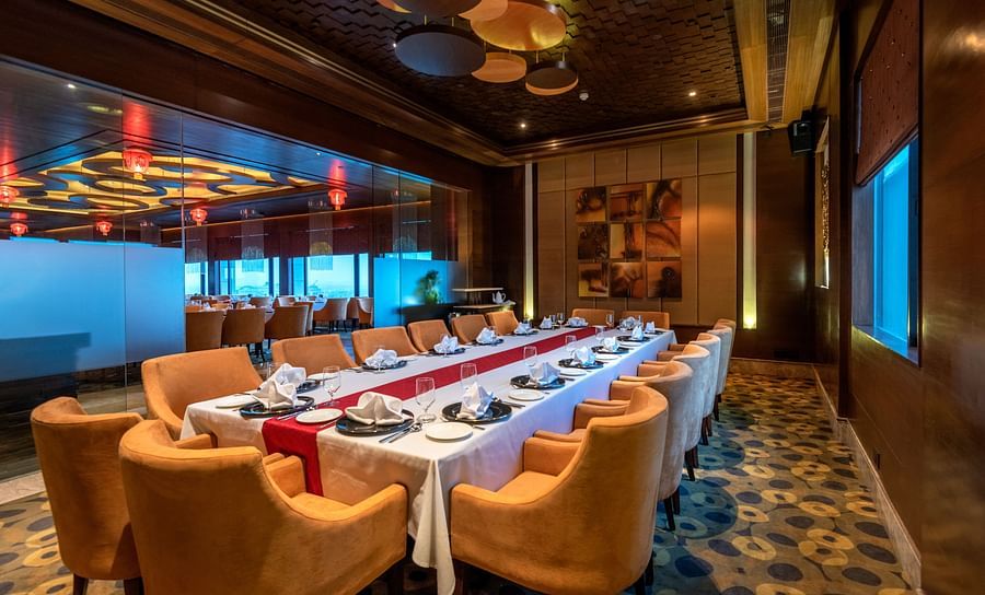An image of a dining area with one huge centre table and several chairs are placed around it - The Suryaa New Delhi