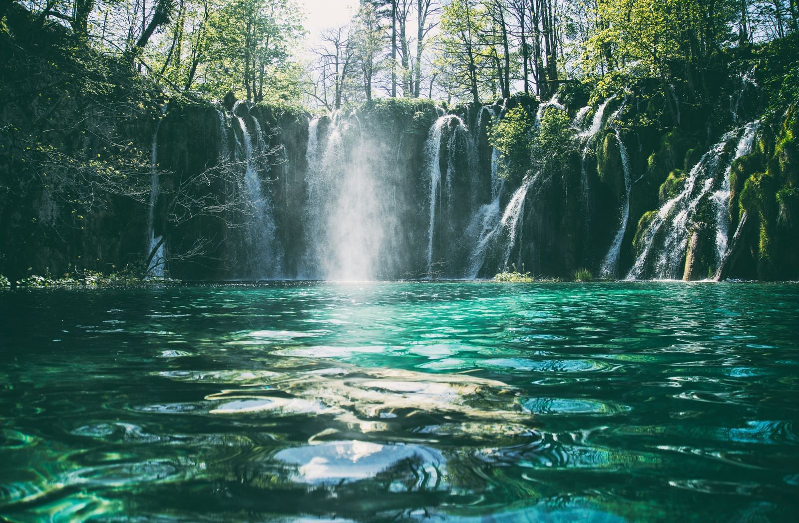 A beautiful, long-exposure shot of a series of terraced waterfalls with bright turquoise pools in a lush, green forest.