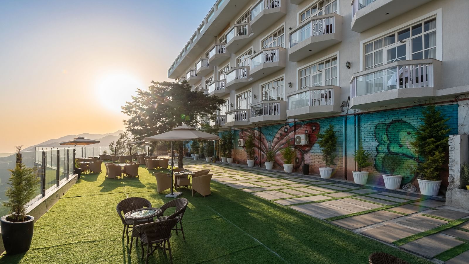 Facade view of DLS Highland Resort and Spa, Mussoorie with comfortable chairs in the lawn at dusk.
