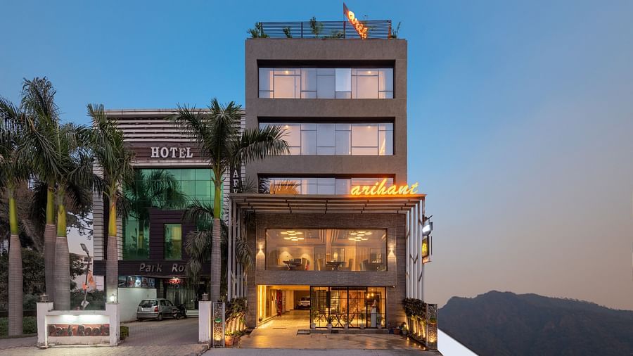 A facade image of DLS Hotel Arihant, Haridwar with trees in front and a mountain in the background