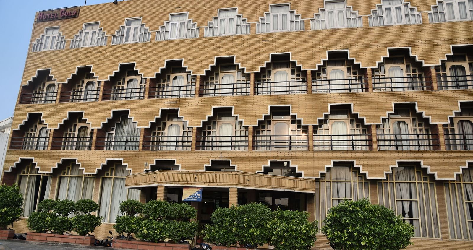 Exterior shot of Hotel Gold, Panipat taken in the morning with dense green bushes in the entrance.
