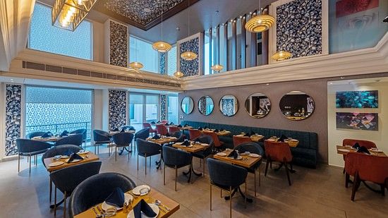 A side view of restaurant dining area with large windows, chairs, artistic wall décor, and ambient ceiling lights at Hotel Saket 27, New Delhi
