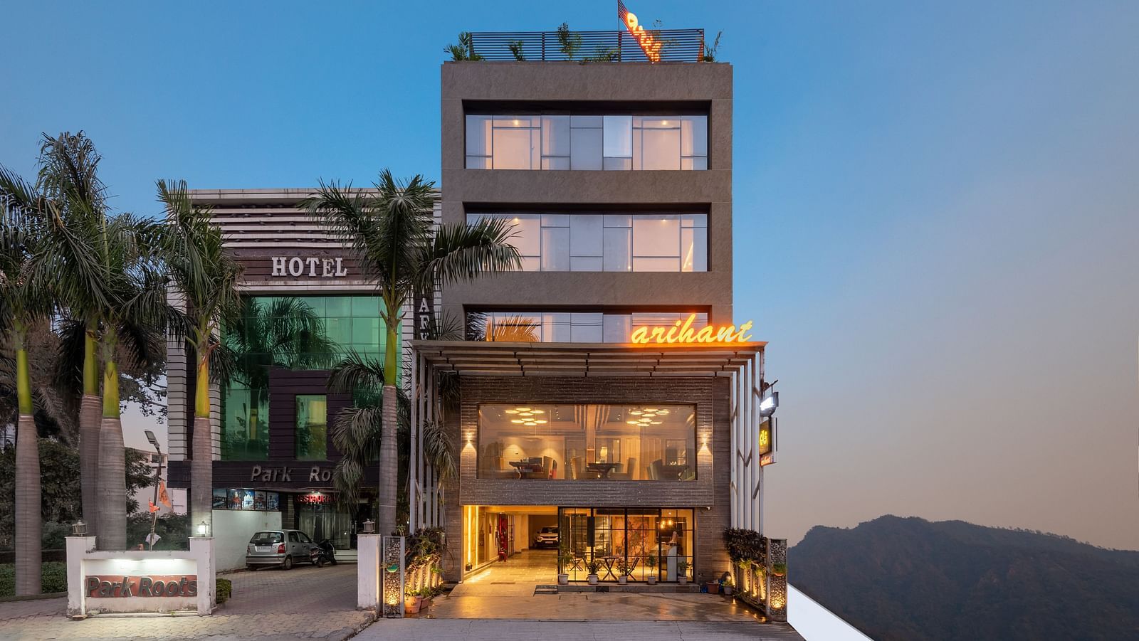 A facade image of DLS Hotel Arihant, Haridwar with trees in front and a mountain in the background