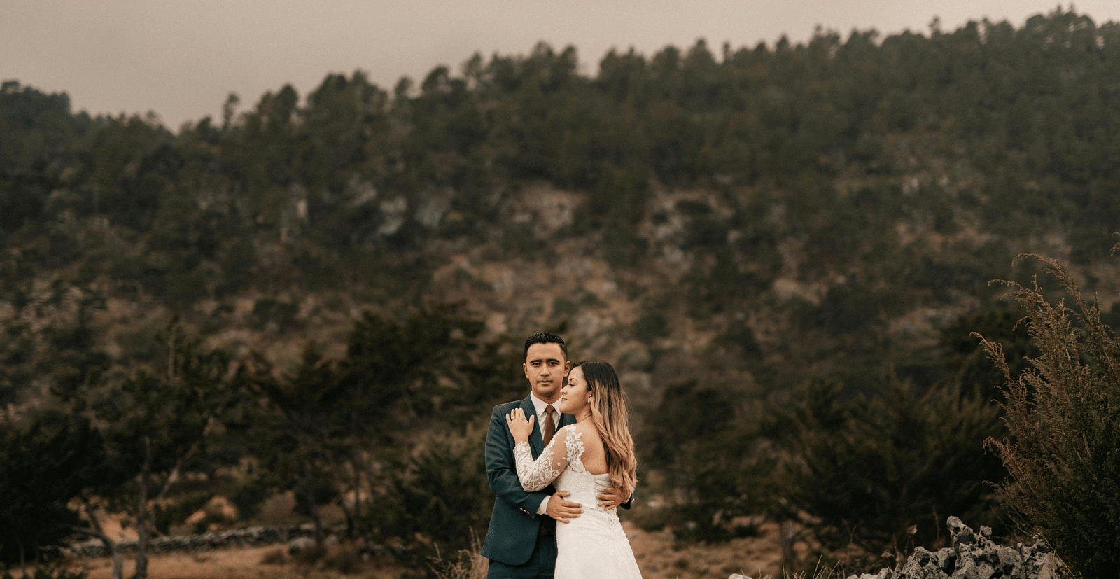 A bride and a groom posing for a photoshoot with a forest in the backdrop - The Groveland Hotel.