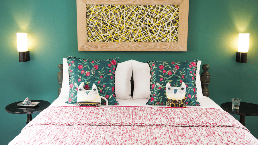 A bed with a pink blanket and two pillows with an owl and a cat printed on them at  Owl and the Pussycat Hotel In Galle.