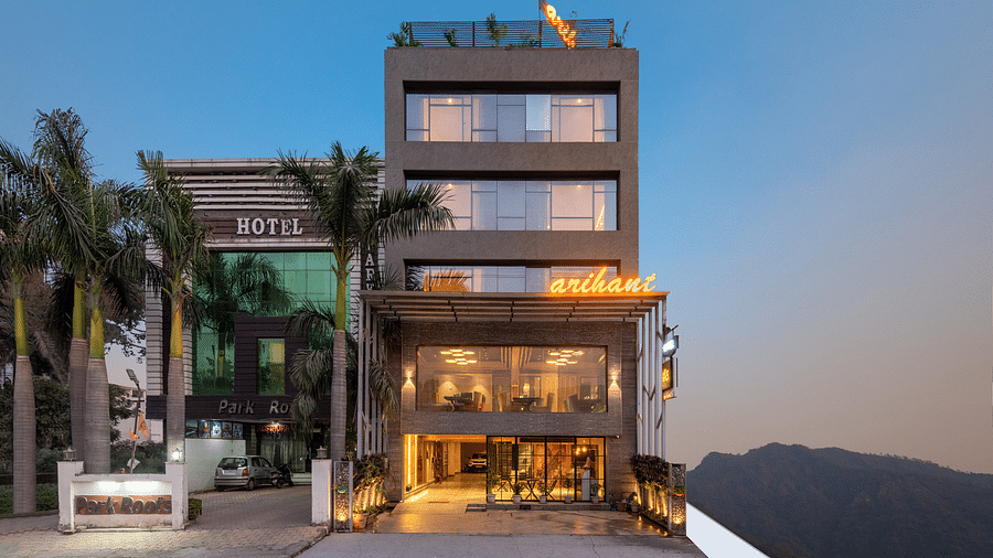 A facade image of DLS Hotel Arihant, Haridwar with trees in front and a mountain in the background
