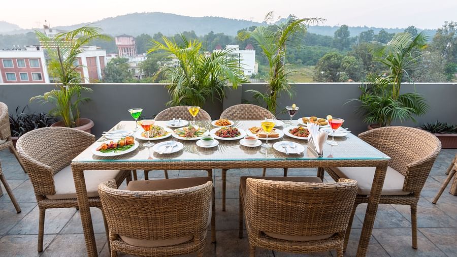 A shot of the dining area on the roof top with a table and chairs and the backdrop of the city view - DLS Hotel Arihant, Haridwar