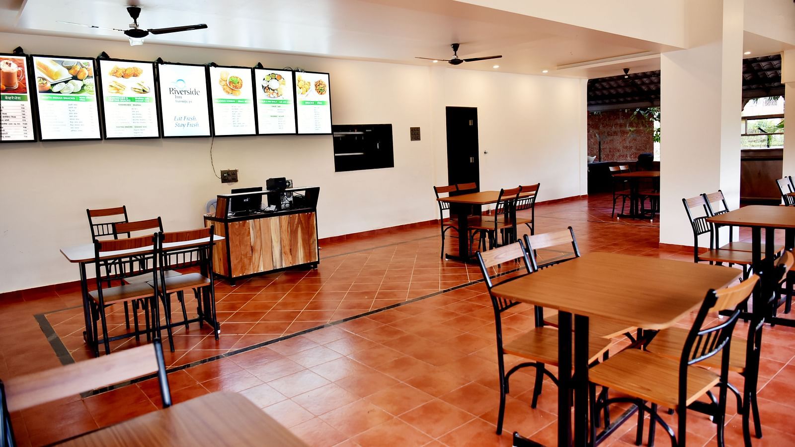 A diagonal view of the dining area at Riverside Inn with tables, chairs, a ceiling fan, and high-level windows.
