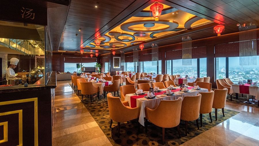 An image of a well lit dining hall where several sets of dining table and chairs are placed - The Suryaa New Delhi