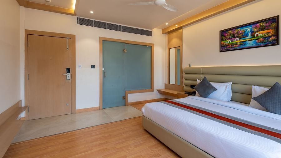 A king size bed in a room along with bed side tables, a full length mirror and other amenities - DLS Hotel Arihant. Haridwar
