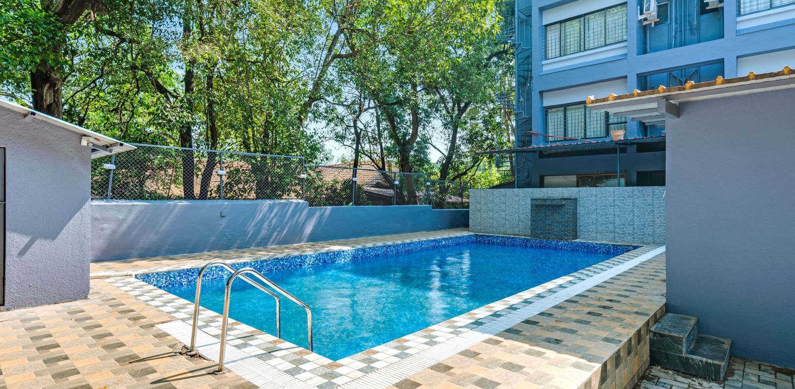 Outdoor swimming pool surrounded by trees and tiled flooring at Emerald Retreat, Tungarli.