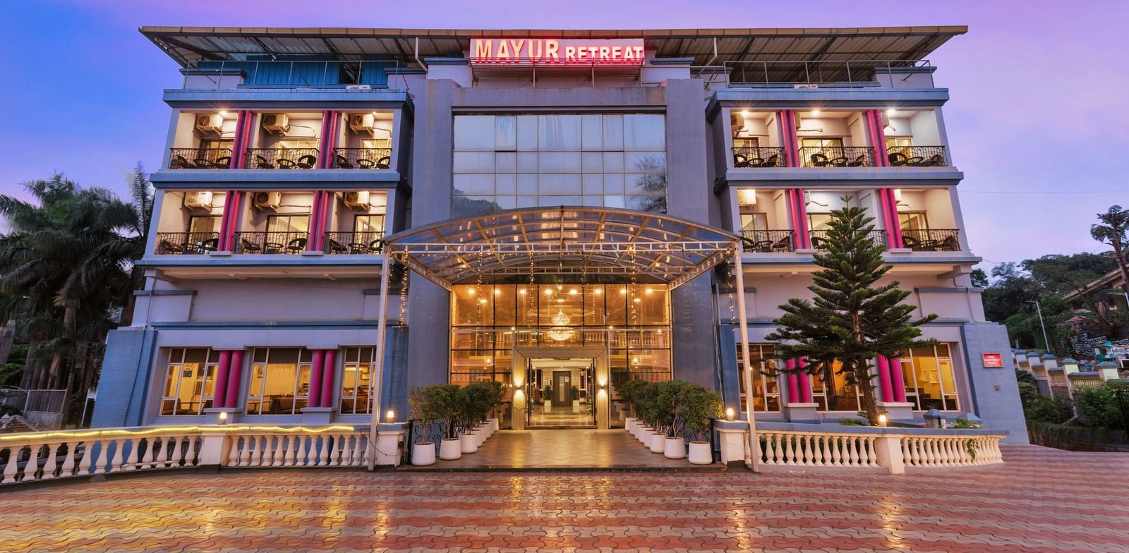 Front view of Mayur Retreat, a modern multi-storey hotel with illuminated glass entrance and symmetrical architecture.