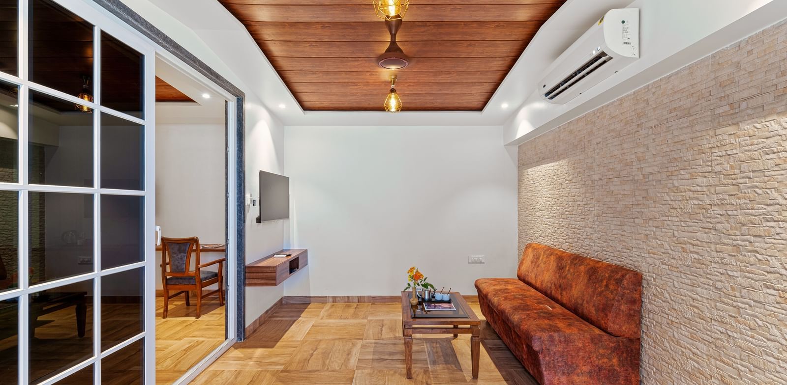 Sitting area at Mayur Retreat with a wooden bench and textured walls, adjoining a bedroom via glass sliding doors.