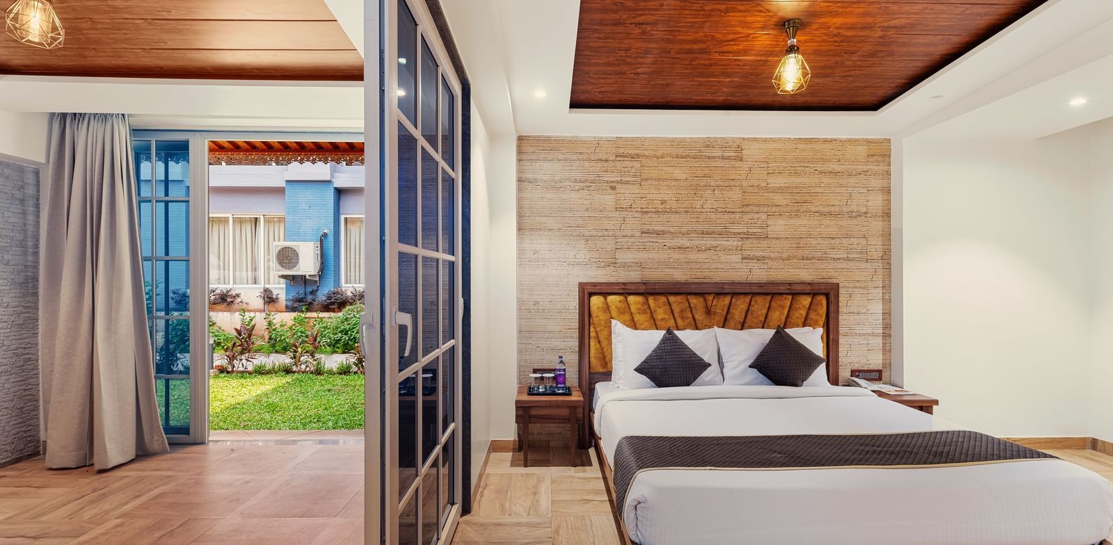 Bright bedroom at Mayur Retreat with a large bed, wooden flooring, and glass doors that open to a private patio.
