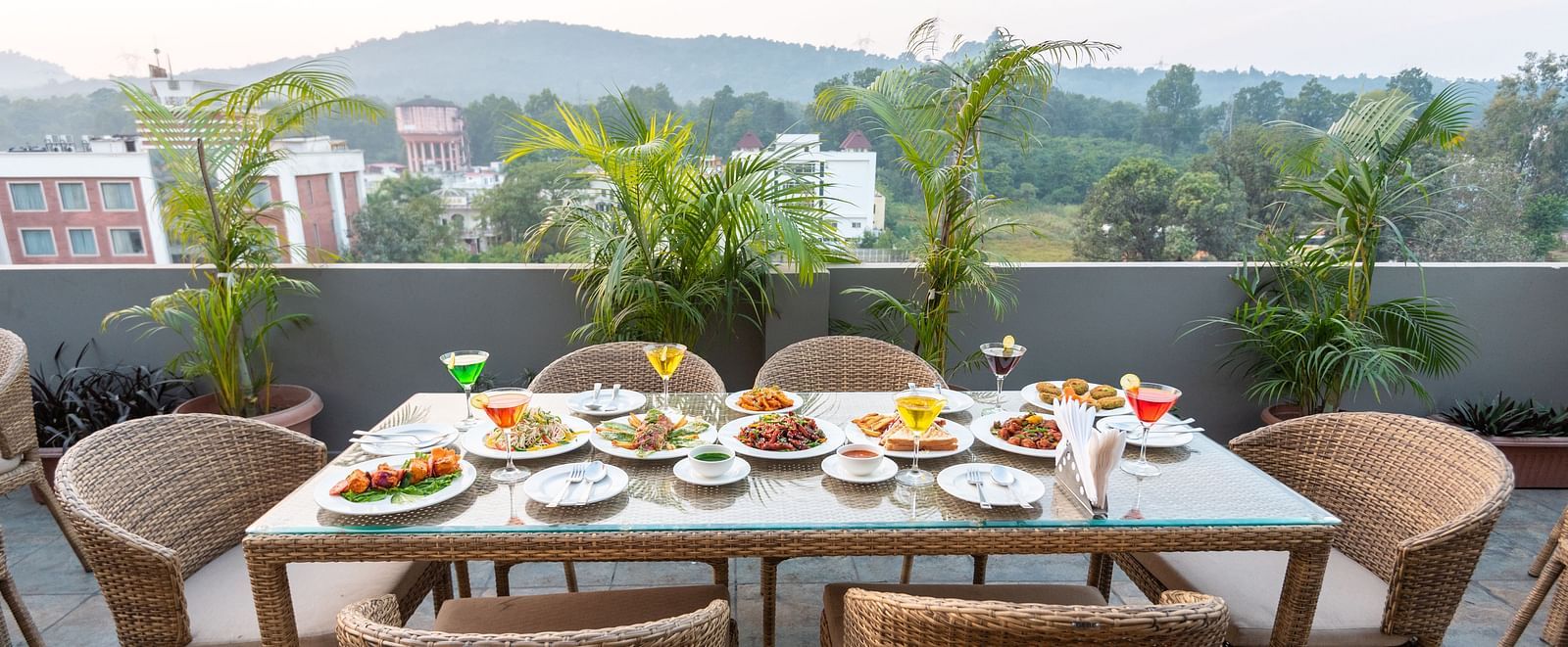 A shot of the dining area on the roof top with a table and chairs and the backdrop of the city view - DLS Hotel Arihant, Haridwar