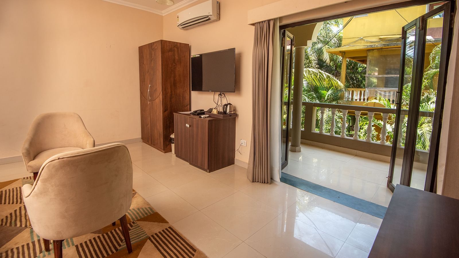 Room with cushioned armchairs, wooden table, TV unit, and sliding glass doors opening to a balcony at De Soul Santé, Morjim.