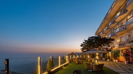 Facade view of DLS Highland Resort and Spa, Mussoorie with comfortable chairs in the lawn at dusk.