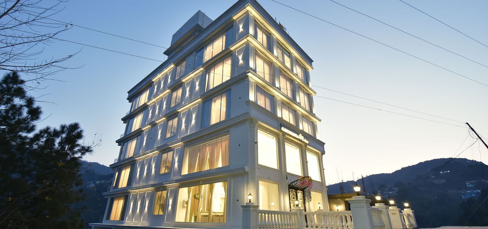 A stunning view of a modern hotel building at night, beautifully illuminated, with an elegant architectural design. The surrounding landscape adds to the serene atmosphere.