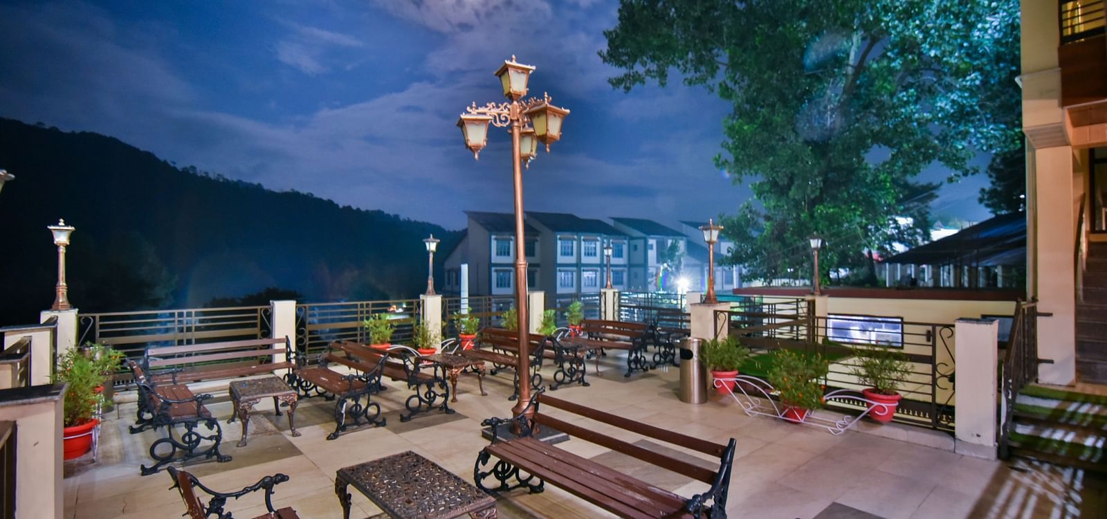 Side view of open terrace at DLS Dalhousie Valley Resort featuring benches and tables during evening.