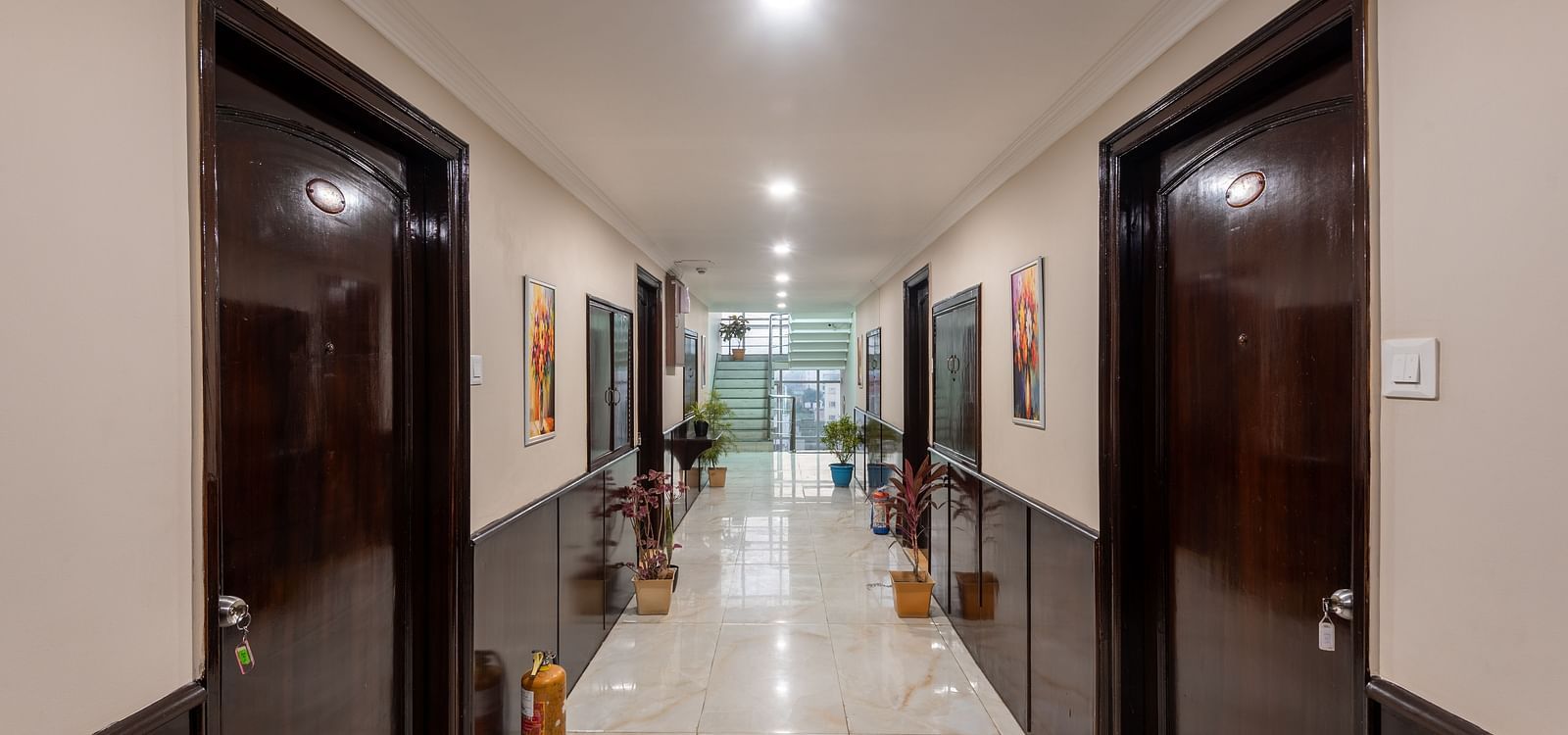 Corridor area at DLS Park Grace, Haridwar multiple doorways to hotel rooms, flight of chairs by the end and bright lighting.