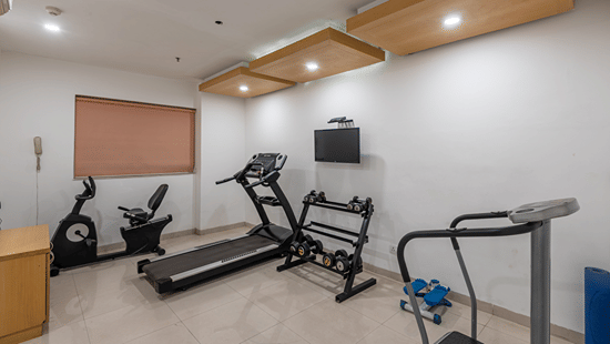Gym with a treadmill and exercise cycles arranged along the wall at Mango Grove Hotel.