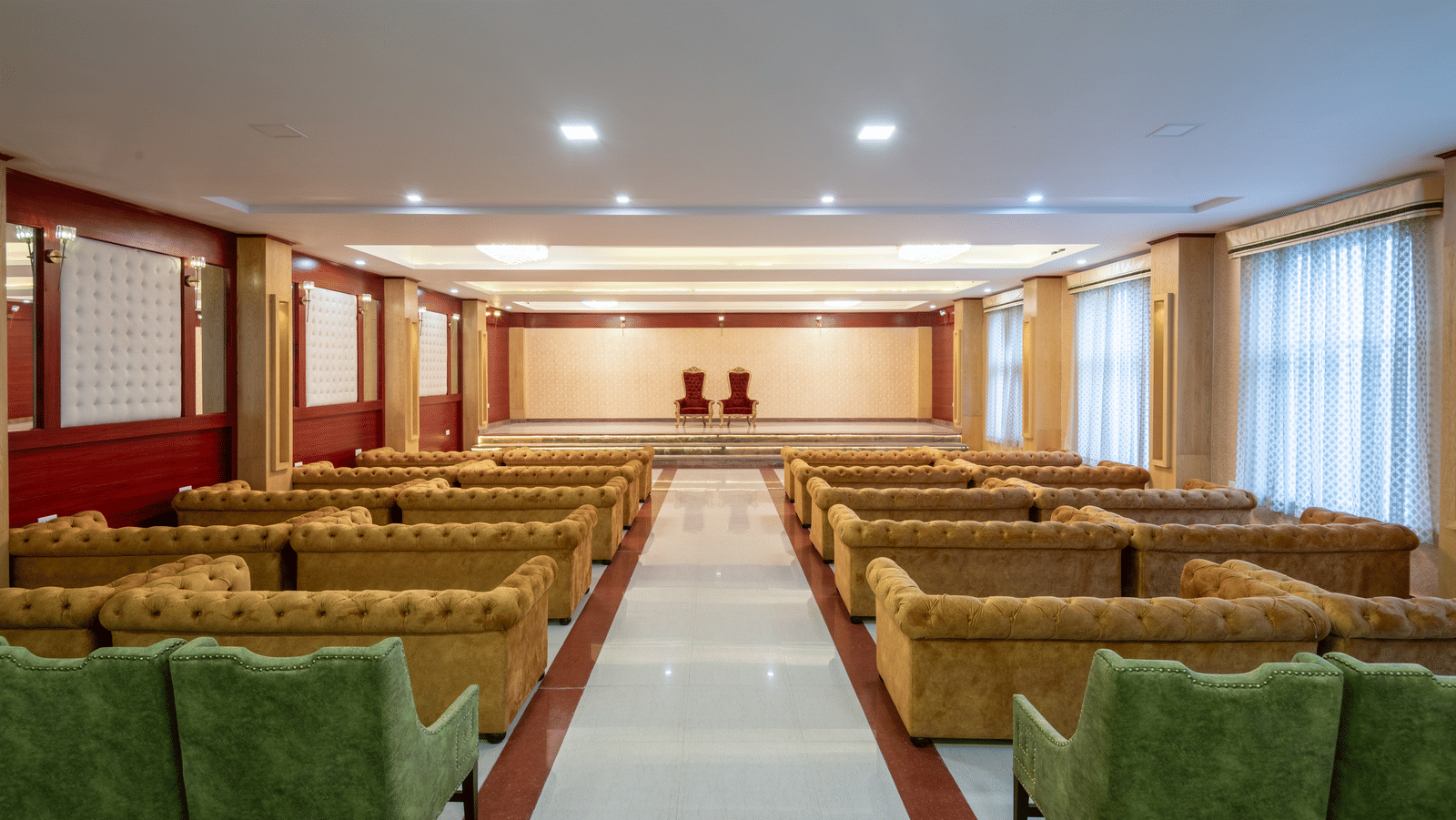 A DLS Hotels banquet hall featuring a combination of sofa and armchair seating facing a stage with 2 ornate chairs.