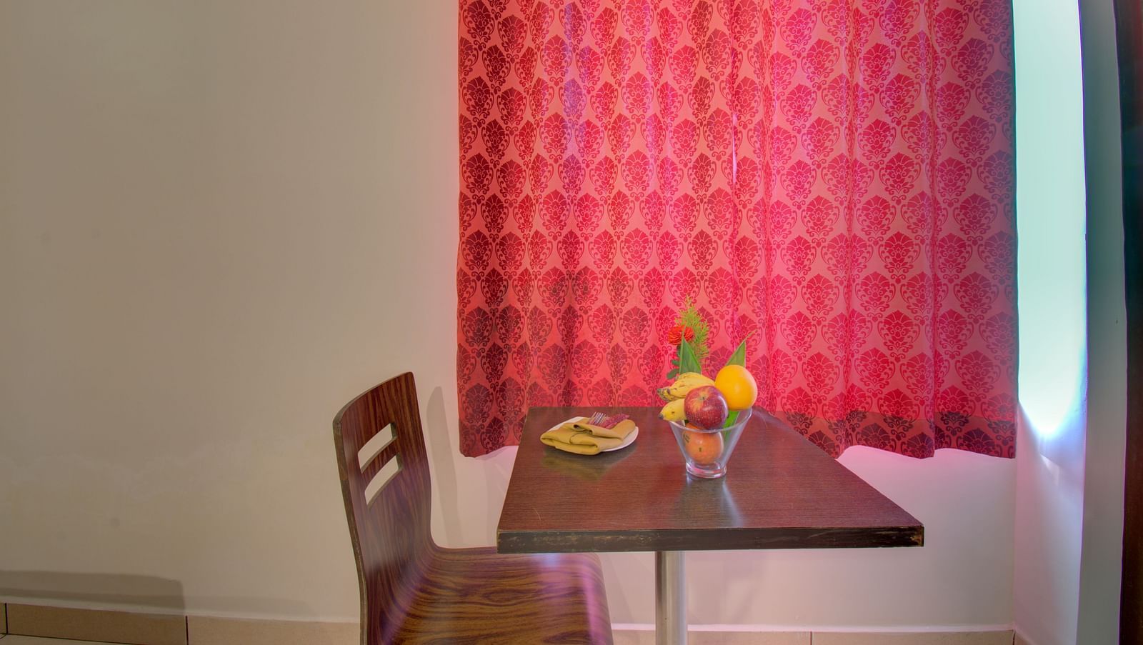 A chair, table with fruits and a curtained window | Superior Room | Woodstock Resorts, Coorg
