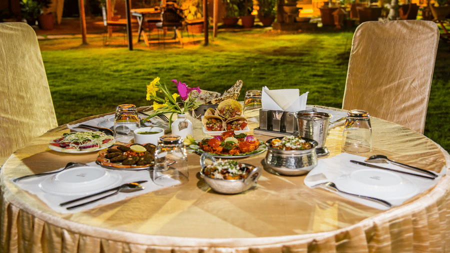 A dining table with multiple dishes and a floral centrepiece on an outdoor lawn at night at Garh Govind.