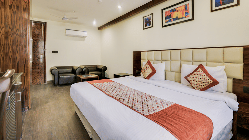 A spacious room with a large, well-made double bed, a cupboard and a seating area beside the door - Hotel Bluestone Prime (Nehru Place), New Delhi