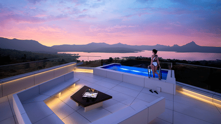 A stunning rooftop deck featuring an illuminated plunge pool and modern lounge seating with a panoramic sunset view of a lake and mountains.