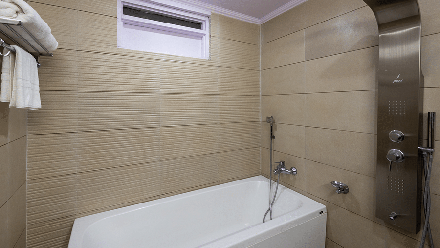 A bathroom with a shower panel, bathtub, and neatly arranged towels on a shelf - DLS Meghavan Resort, Dharamshala