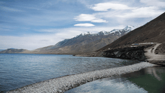 A vast water body surrounded by towering mountains on the sides and in the background.