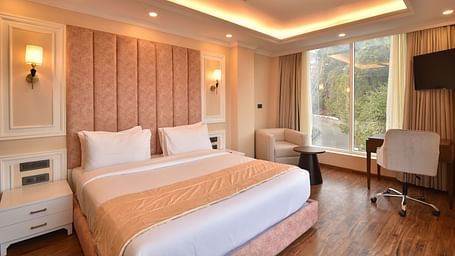 A modern hotel room with a king-sized bed, featuring soft lighting and large windows that offer stunning views of the surrounding hills and landscape.