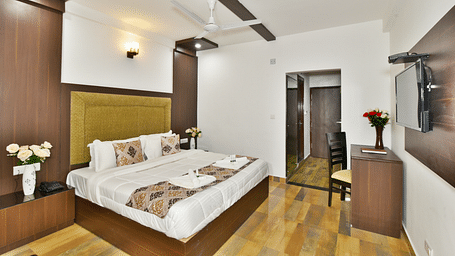 The spacious and well lit guest room that features a comfortable bed, a work desk, and a modern aesthetic | DLS Kapoor Resort Manali