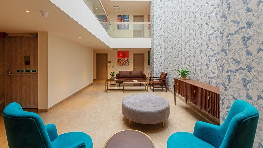 A hotel living area with sofas, tables, painted decorative well with doors and with the first floor balconies visible at Hotel Saket 27, New Delhi