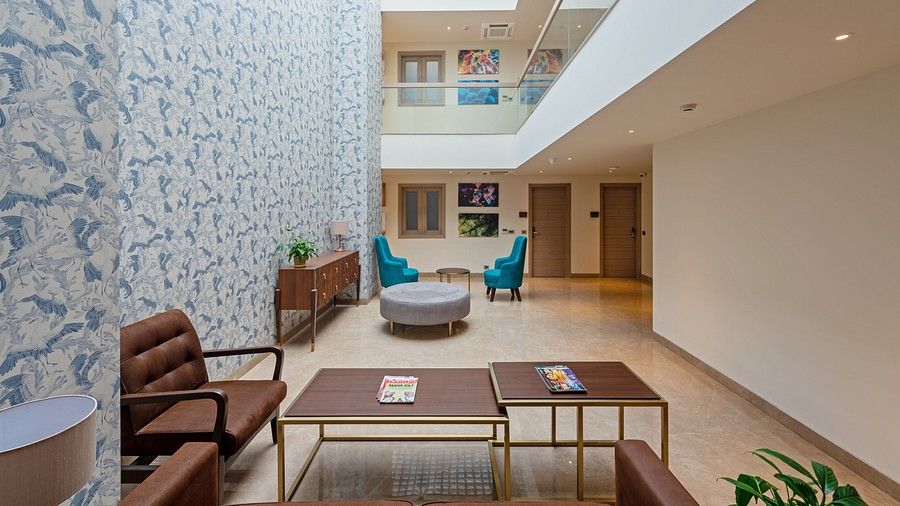 A side view of a living area with sofas, tables, doors and upper-floor pathways at Hotel Saket 27, New Delhi