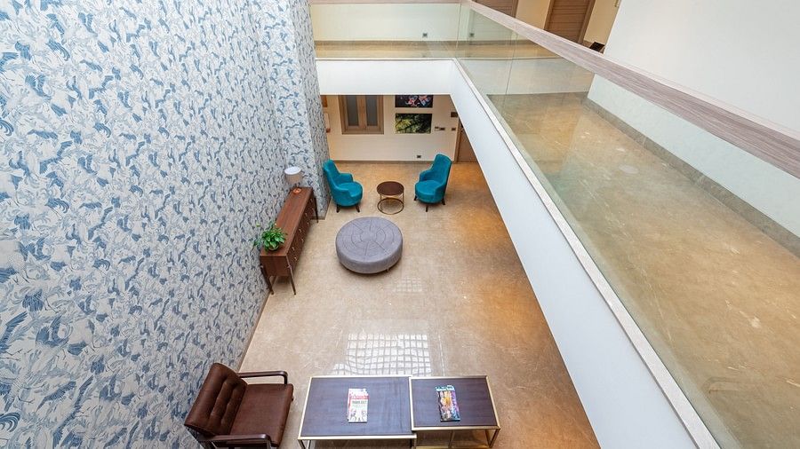 A top view from the first floor balcony of a spacious living area with sofas, table, decorative wall and doors to rooms at Hotel Saket 27, New Delhi
