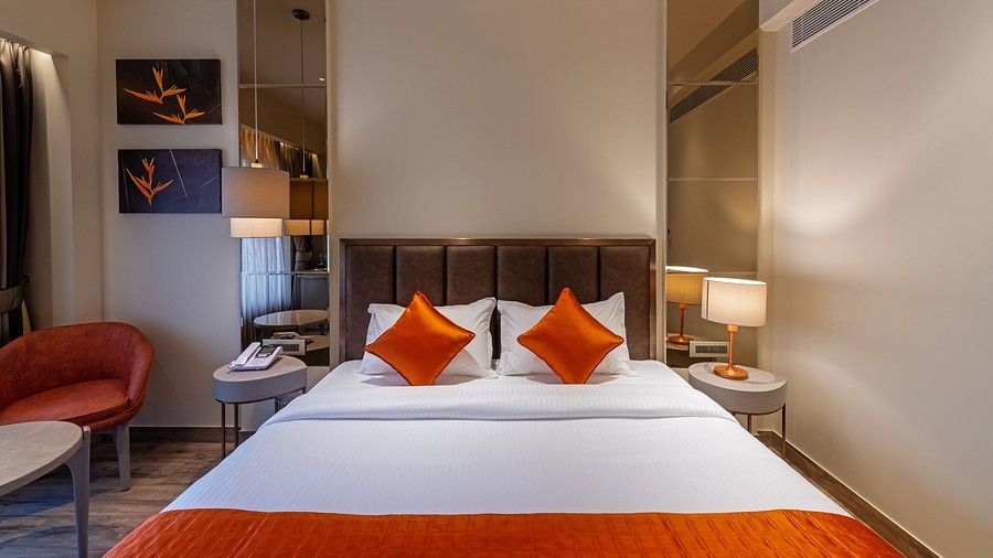 A double bed room with pillows, chairs, side table with lamp, phone and warm lighting at Hotel Saket 27, New Delhi