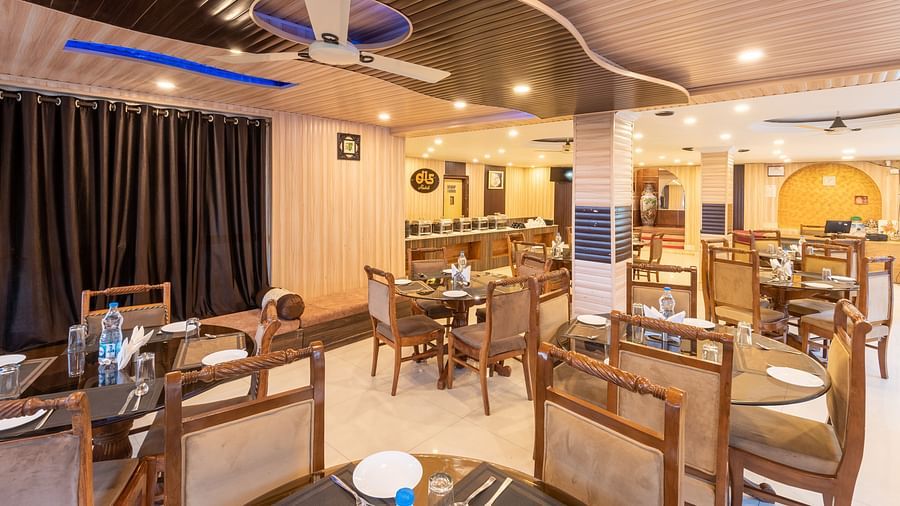A dining area in Anupam Resort. The room features round tables with white tablecloths, wooden chairs, and dark curtains | DLS Anupam Resort, Dharamshala