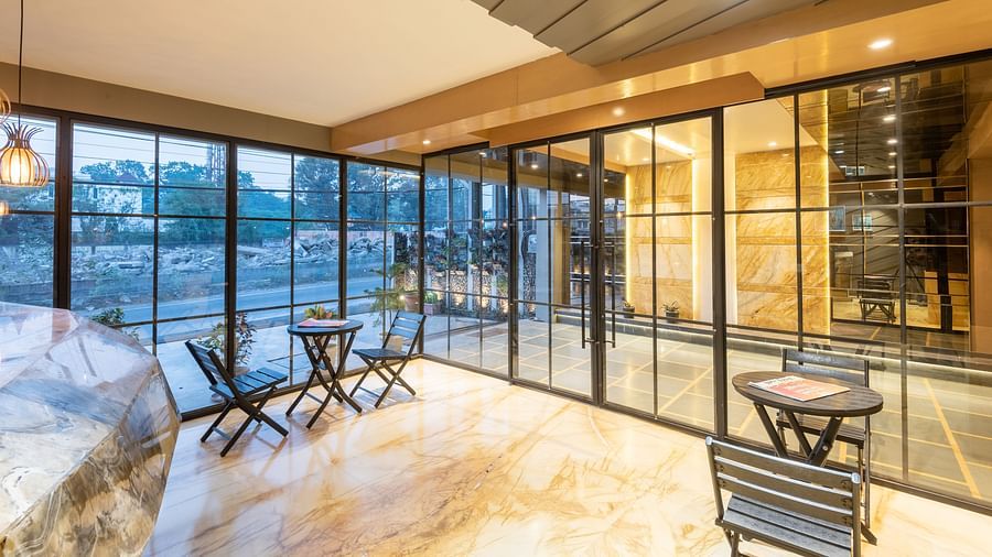 The waiting area of DLS Hotel Arihant, Haridwar featuring chairs and tables with huge glass door in the background